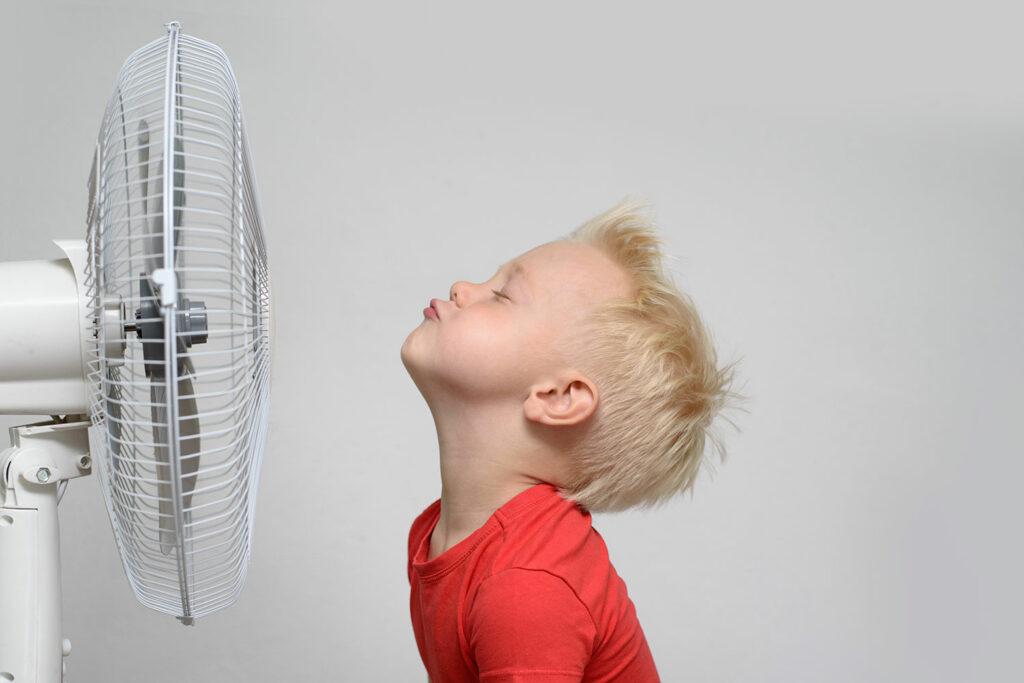 Image of boy trying to stay cool with an air conditioner