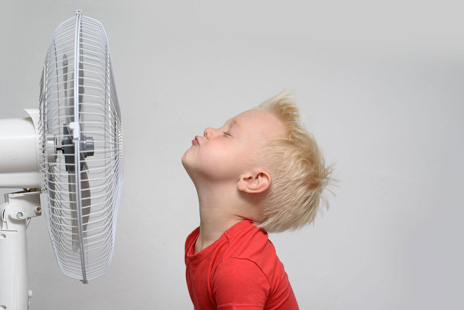 Image of boy trying to stay cool with an air conditioner