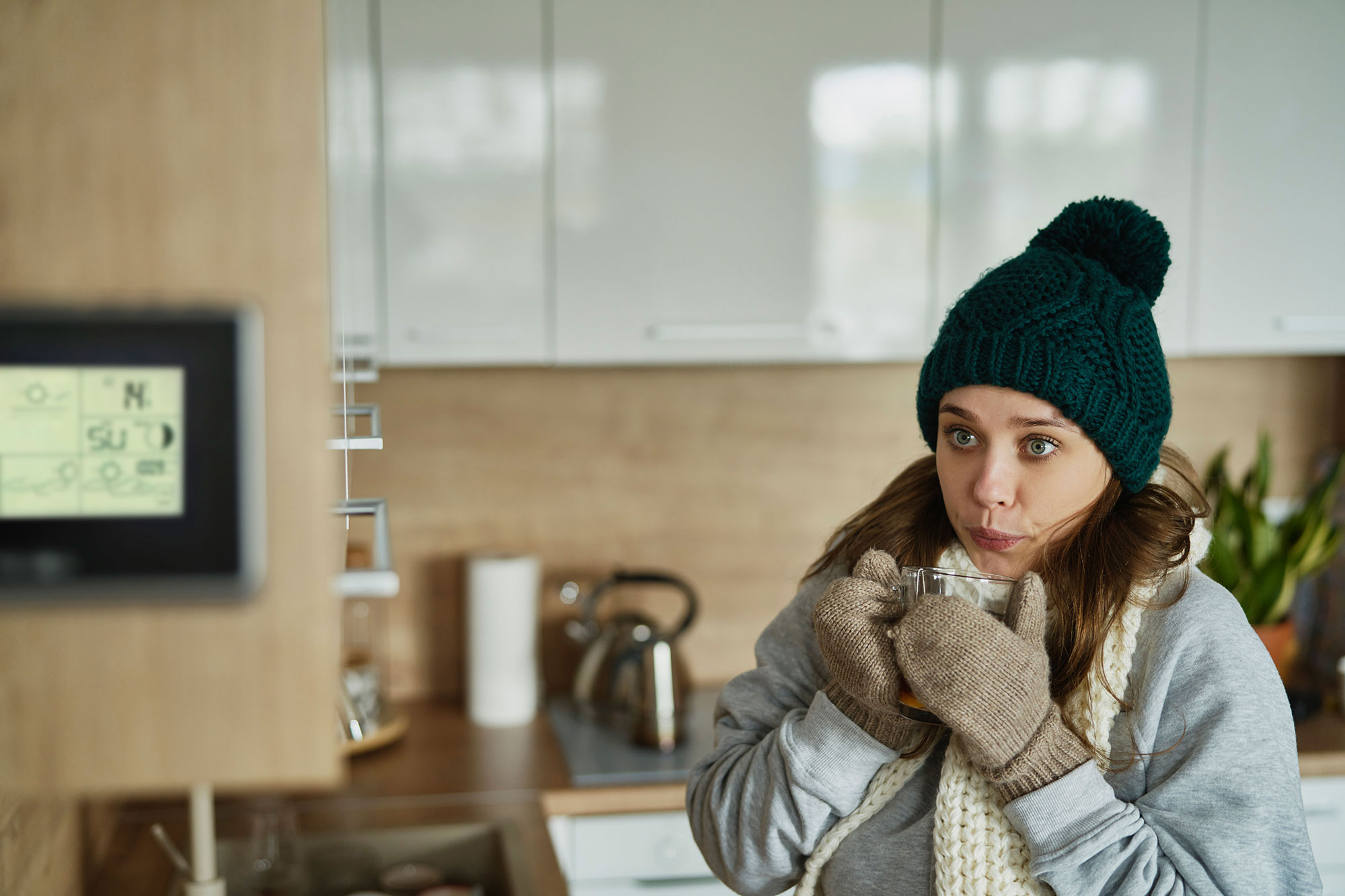 woman at home drinking coffee is cold and looking at thermostat