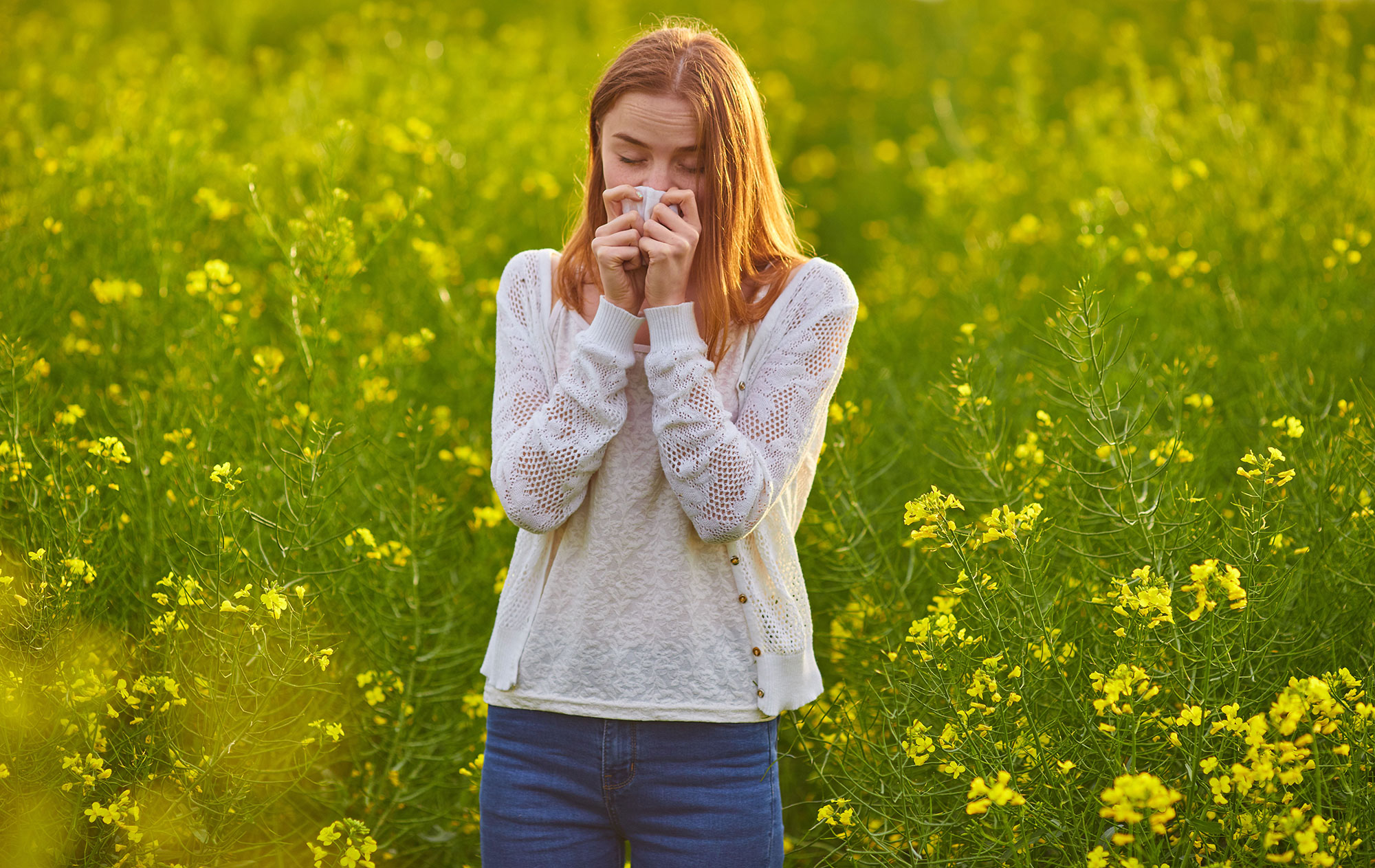 Woman standing in a field of flowers and being affected by allergies
